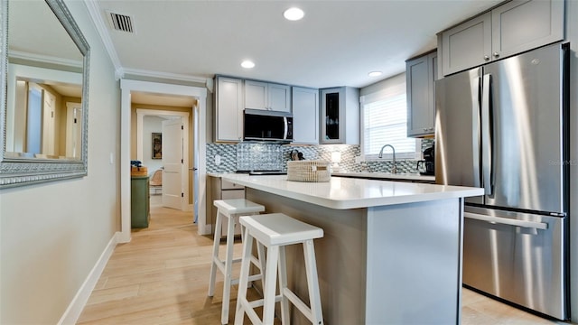 kitchen with a breakfast bar area, gray cabinetry, stainless steel appliances, light countertops, and tasteful backsplash