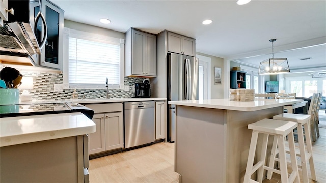 kitchen with a breakfast bar, gray cabinetry, backsplash, appliances with stainless steel finishes, and light countertops