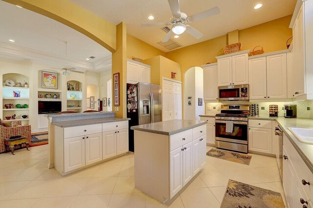 7762 US Open Loop, Lakewood Ranch, FL 34202 - kitchen with appliances with stainless steel finishes, a ceiling fan, arched walkways, a center island, and white cabinetry