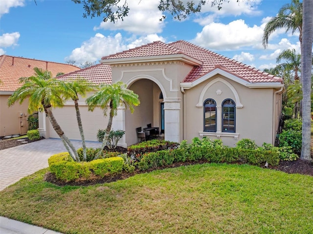 mediterranean / spanish house featuring decorative driveway, a tile roof, stucco siding, an attached garage, and a front yard