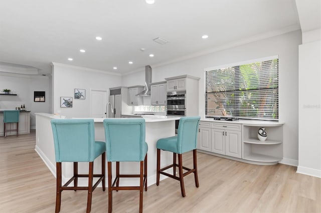 kitchen featuring light wood finished floors, decorative backsplash, appliances with stainless steel finishes, light countertops, and wall chimney range hood