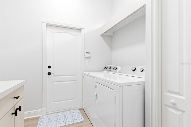 laundry area with light wood-type flooring, washing machine and clothes dryer, and cabinet space