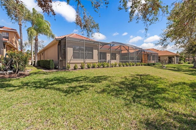 rear view of house featuring a lawn, a tile roof, a lanai, and stucco siding