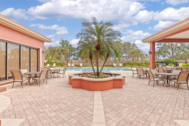 view of patio with a community pool, fence, and outdoor dining area