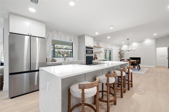 kitchen with appliances with stainless steel finishes, light wood-type flooring, a kitchen island, and white cabinetry