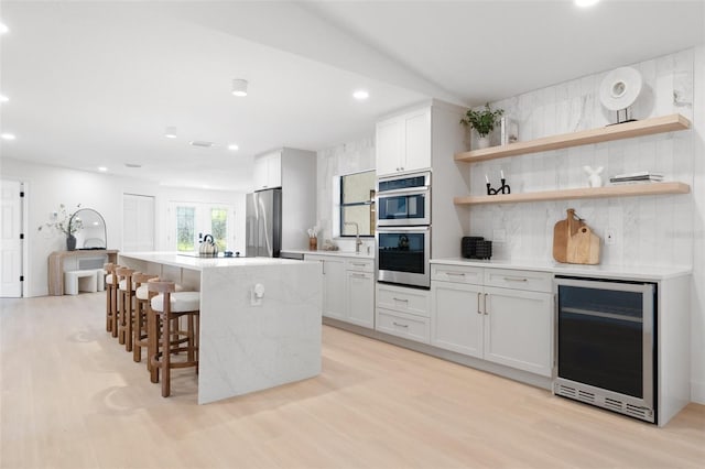 kitchen featuring light wood-type flooring, wine cooler, appliances with stainless steel finishes, and light countertops