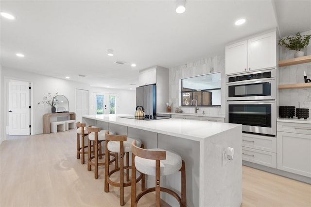 kitchen with stainless steel appliances, light countertops, a kitchen island, a sink, and light wood-type flooring