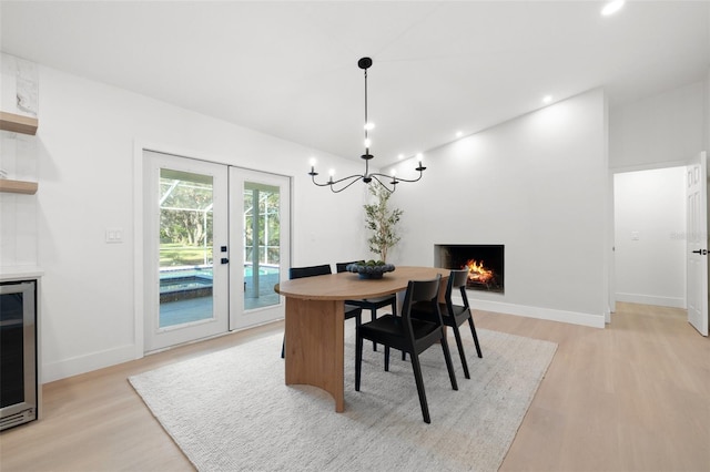 dining room with a warm lit fireplace, wine cooler, recessed lighting, french doors, and light wood-type flooring