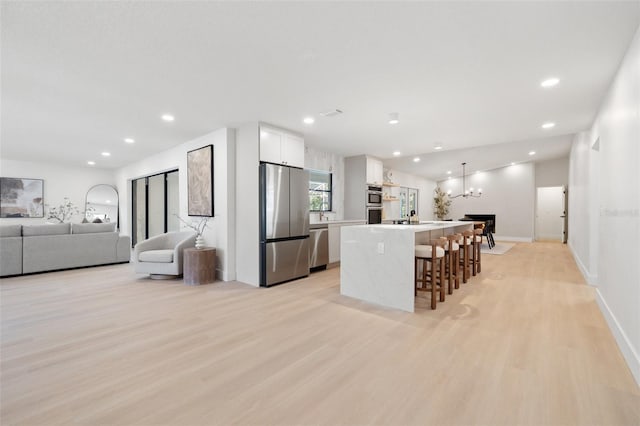 kitchen with a breakfast bar, light wood finished floors, appliances with stainless steel finishes, open floor plan, and white cabinetry