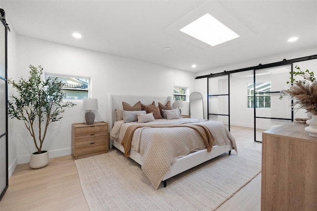 bedroom with a skylight, recessed lighting, light wood-style flooring, a barn door, and baseboards