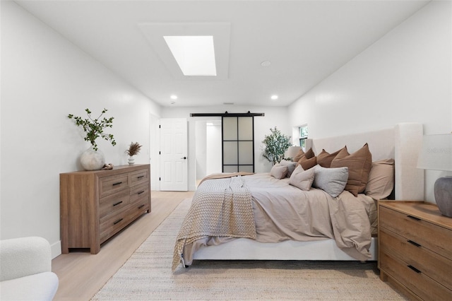 bedroom featuring a skylight, light wood-style flooring, recessed lighting, and a barn door