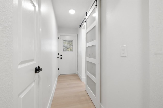 hall with light wood-style floors, a barn door, and baseboards