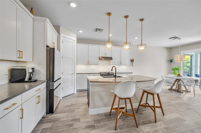 kitchen featuring a breakfast bar area, light wood-style flooring, a sink, visible vents, and white cabinetry