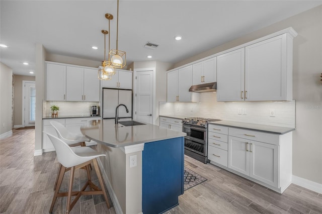 kitchen featuring light wood finished floors, range with two ovens, white fridge, under cabinet range hood, and a sink