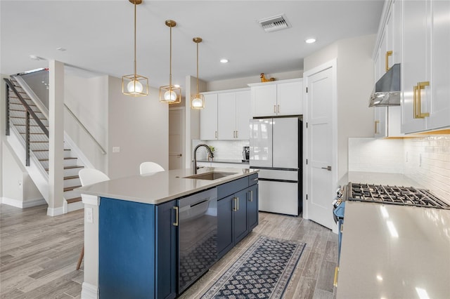 kitchen featuring light wood-style flooring, appliances with stainless steel finishes, blue cabinetry, under cabinet range hood, and a sink