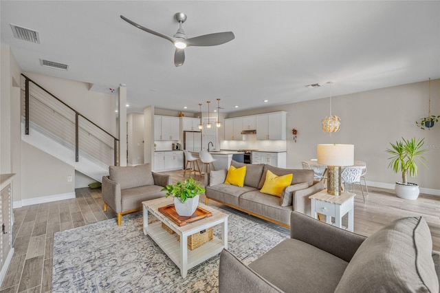 living room featuring light wood-type flooring, visible vents, stairway, and baseboards