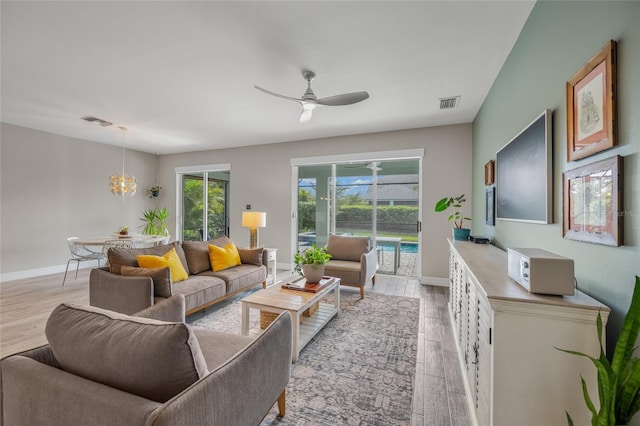 living area featuring ceiling fan with notable chandelier, light wood-type flooring, visible vents, and baseboards