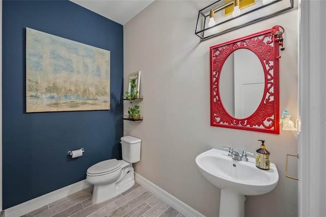 half bath featuring baseboards, a sink, toilet, and wood tiled floor