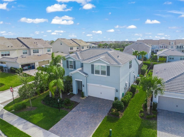 view of front of house featuring a garage, a tile roof, a residential view, decorative driveway, and a front lawn