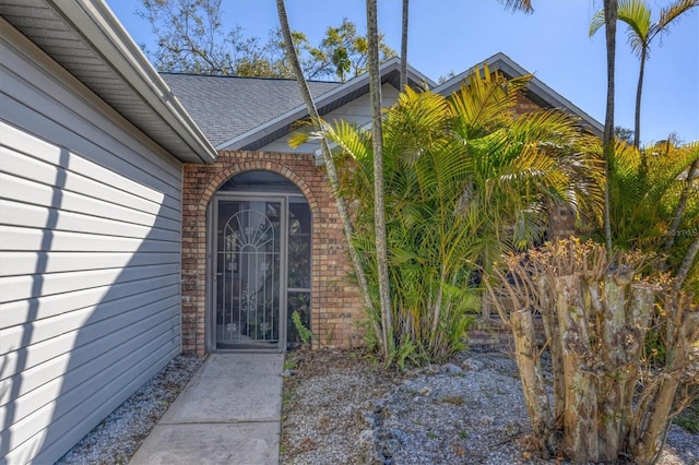 entrance to property featuring a shingled roof and brick siding