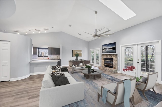 living area with a ceiling fan, vaulted ceiling with skylight, light wood-style flooring, and baseboards