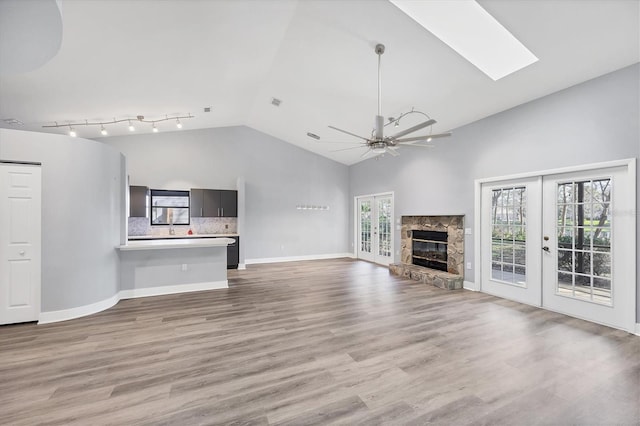 unfurnished living room with baseboards, a ceiling fan, french doors, a stone fireplace, and light wood-style floors