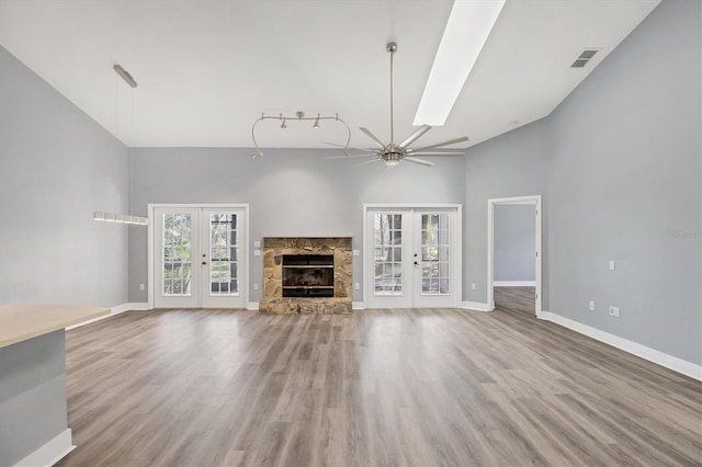 unfurnished living room featuring french doors, visible vents, a stone fireplace, and baseboards