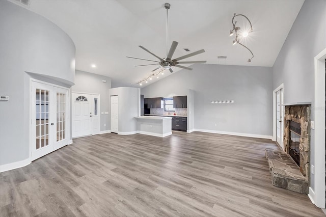 unfurnished living room featuring french doors, a stone fireplace, wood finished floors, high vaulted ceiling, and baseboards