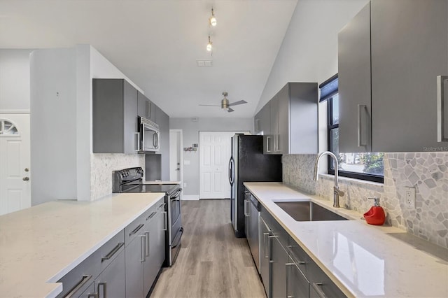 kitchen with appliances with stainless steel finishes, gray cabinets, a sink, and light stone counters