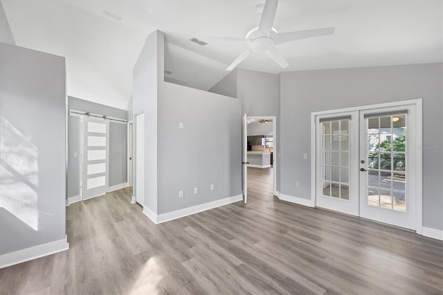 unfurnished living room featuring french doors, lofted ceiling, a barn door, ceiling fan, and wood finished floors