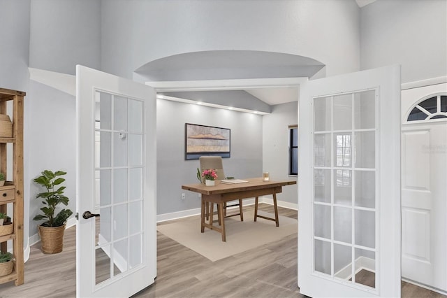 office area featuring baseboards, arched walkways, wood finished floors, and french doors