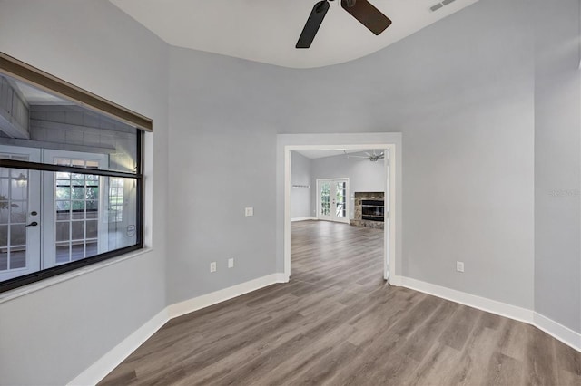 empty room featuring a fireplace, wood finished floors, a ceiling fan, and baseboards