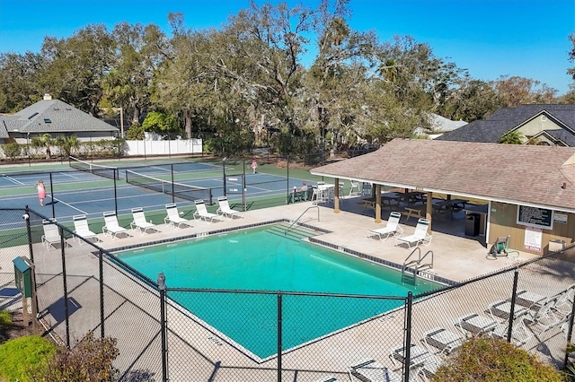 community pool featuring a tennis court, a patio area, and fence