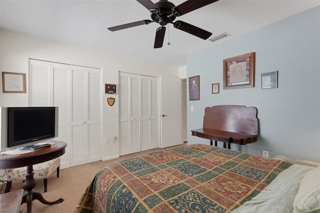 carpeted bedroom with a textured ceiling, ceiling fan, visible vents, and multiple closets