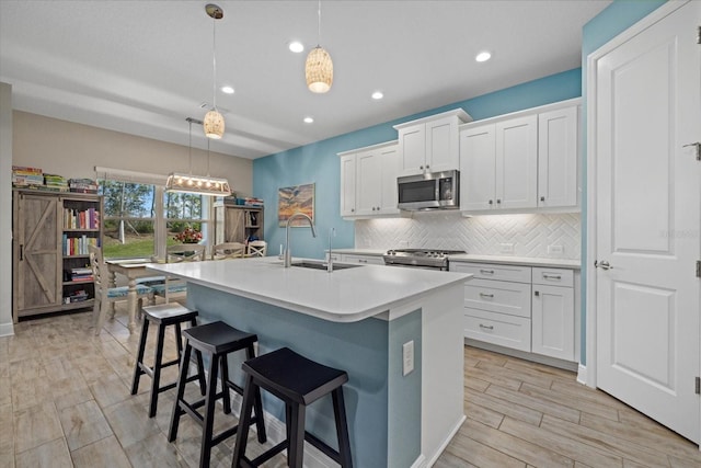 kitchen featuring a center island with sink, stainless steel appliances, light countertops, decorative backsplash, and a sink