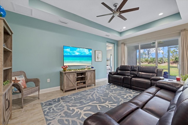 living room with visible vents, a ceiling fan, baseboards, light wood finished floors, and a raised ceiling