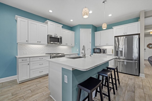 kitchen with a kitchen island with sink, stainless steel appliances, a kitchen bar, white cabinetry, and a sink