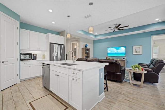 kitchen featuring stainless steel appliances, backsplash, open floor plan, white cabinetry, and a sink