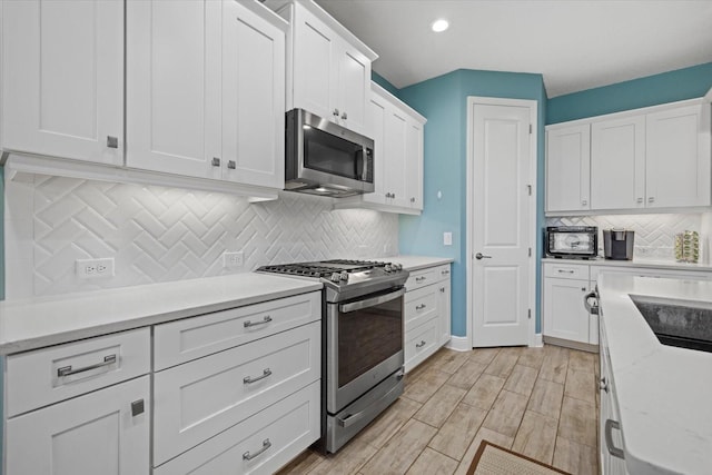 kitchen with light wood finished floors, stainless steel appliances, light countertops, decorative backsplash, and white cabinetry