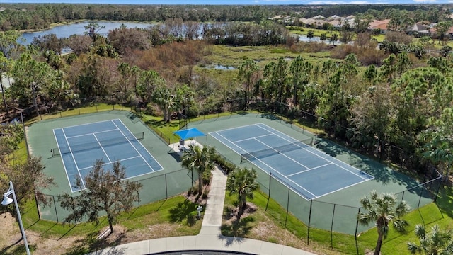 view of tennis court featuring a water view, fence, and a view of trees