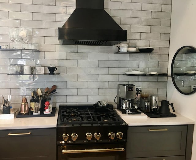 kitchen with tasteful backsplash, light countertops, wall chimney range hood, and black gas range oven