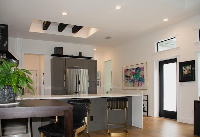 kitchen with recessed lighting, light countertops, light wood-style floors, freestanding refrigerator, and a kitchen breakfast bar