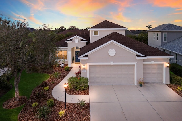 traditional-style home with a shingled roof, concrete driveway, an attached garage, and stucco siding