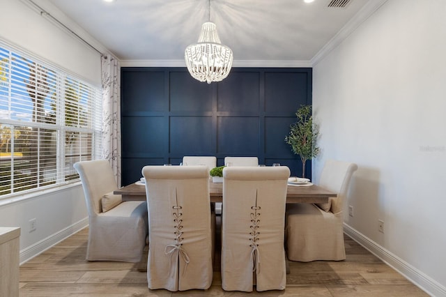 dining space featuring a notable chandelier, a decorative wall, light wood-style floors, baseboards, and crown molding