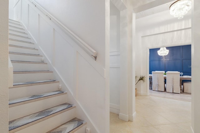 stairway featuring a decorative wall, a notable chandelier, and tile patterned floors