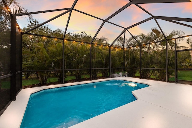 pool at dusk with a patio, glass enclosure, and an outdoor pool