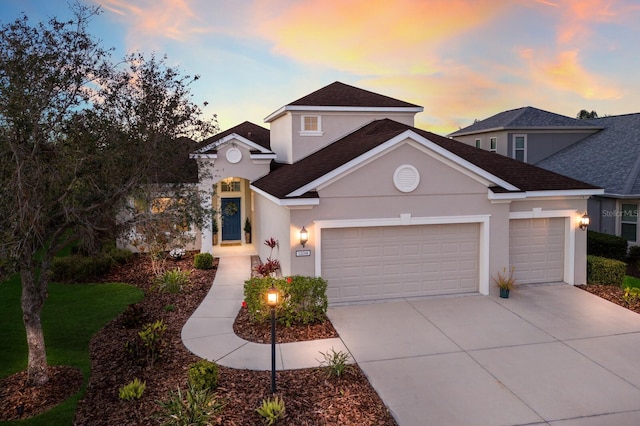 traditional-style house with an attached garage, driveway, a shingled roof, and stucco siding