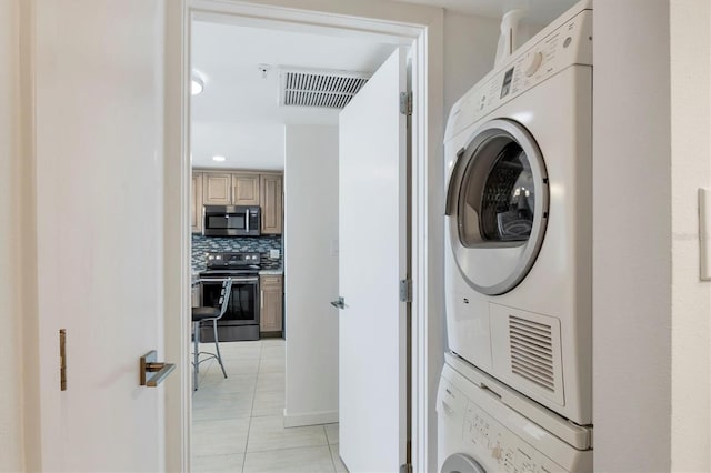 laundry room with light tile patterned flooring, stacked washer and clothes dryer, visible vents, and laundry area