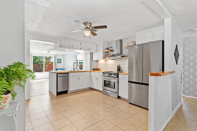 kitchen featuring wall chimney exhaust hood, appliances with stainless steel finishes, a peninsula, white cabinetry, and a sink