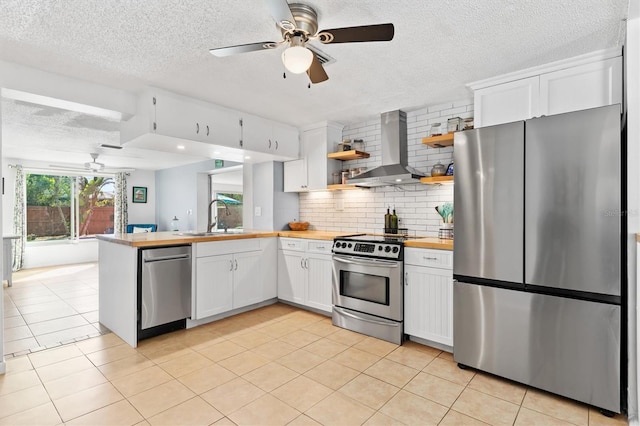 kitchen featuring open shelves, appliances with stainless steel finishes, a sink, a peninsula, and wall chimney exhaust hood